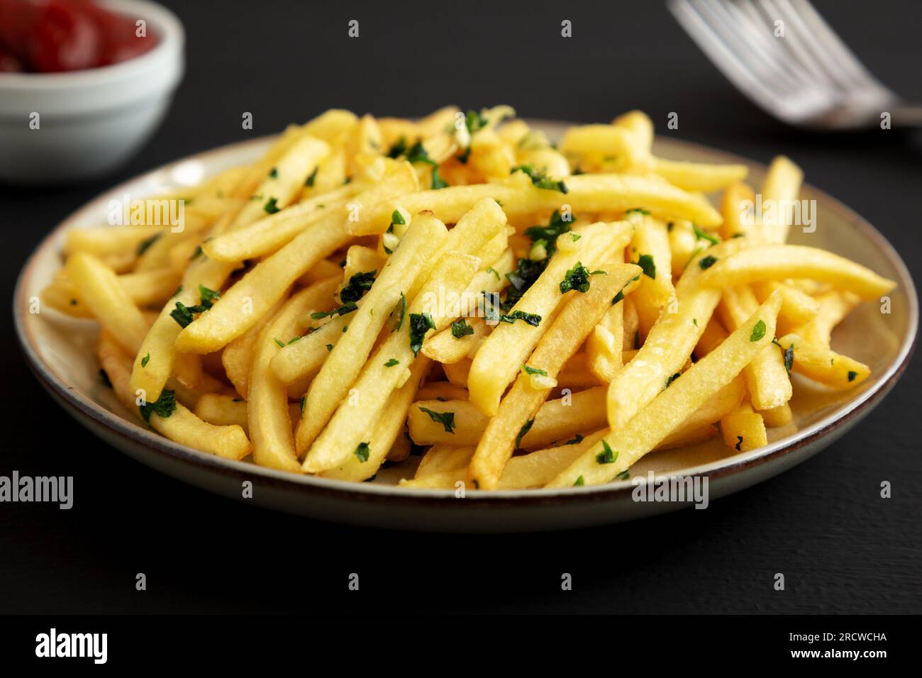Garlic French Fries with Parsley on a Plate on a black background, side