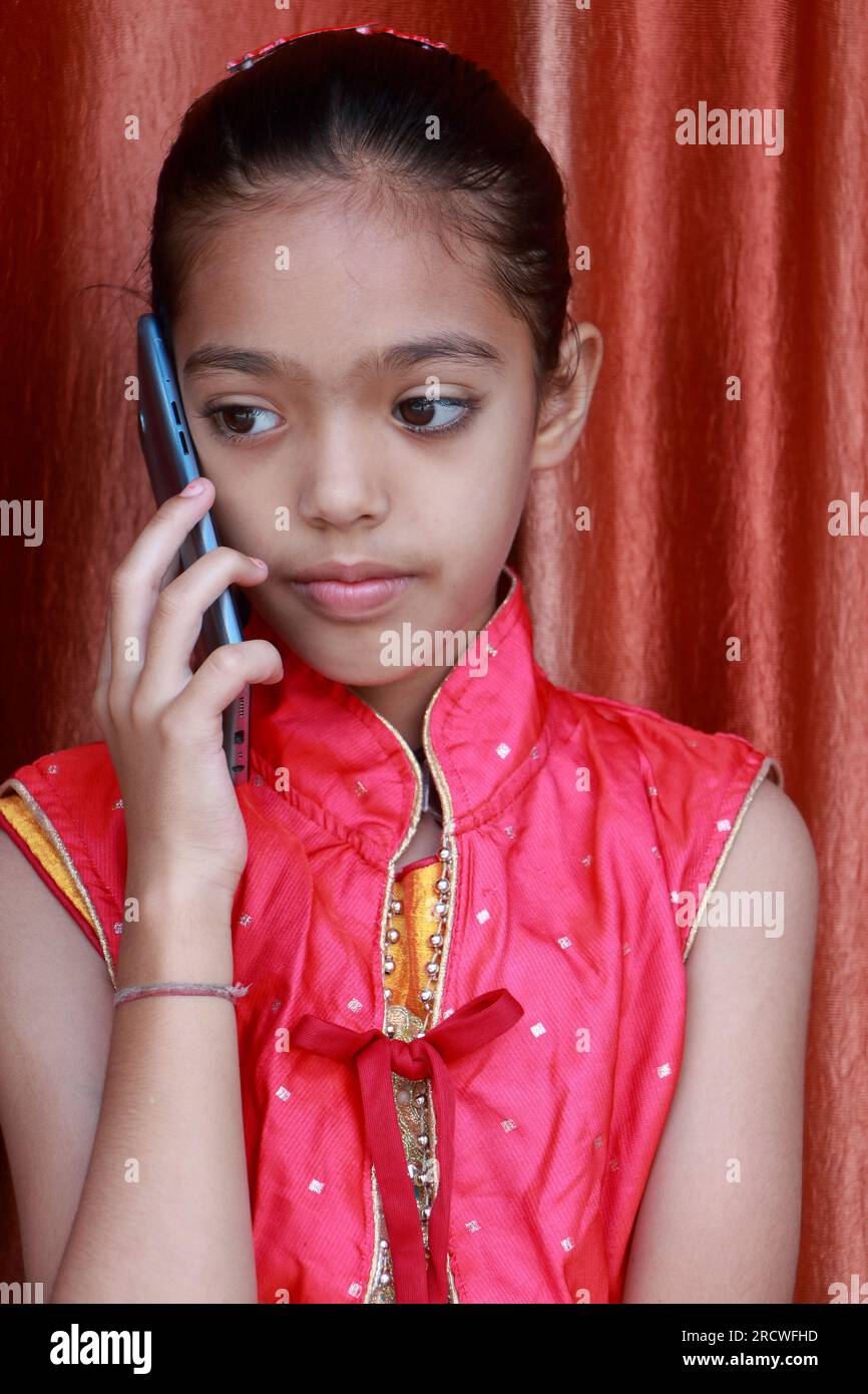 An Indian little pretty girl talking on a mobile phone in various poses in red dress. Stock Photo