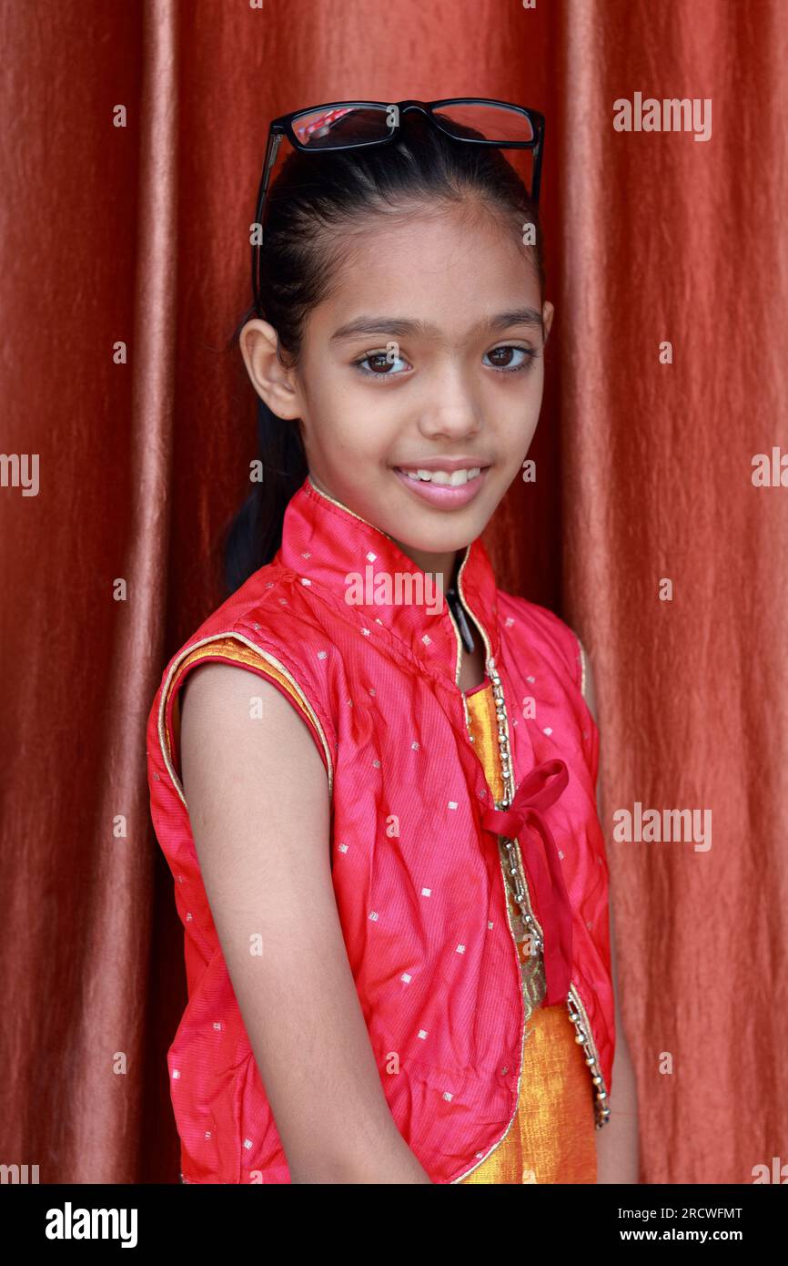 An Indian little pretty girl fiddling with her eye glasses in various poses in red dress. Stock Photo