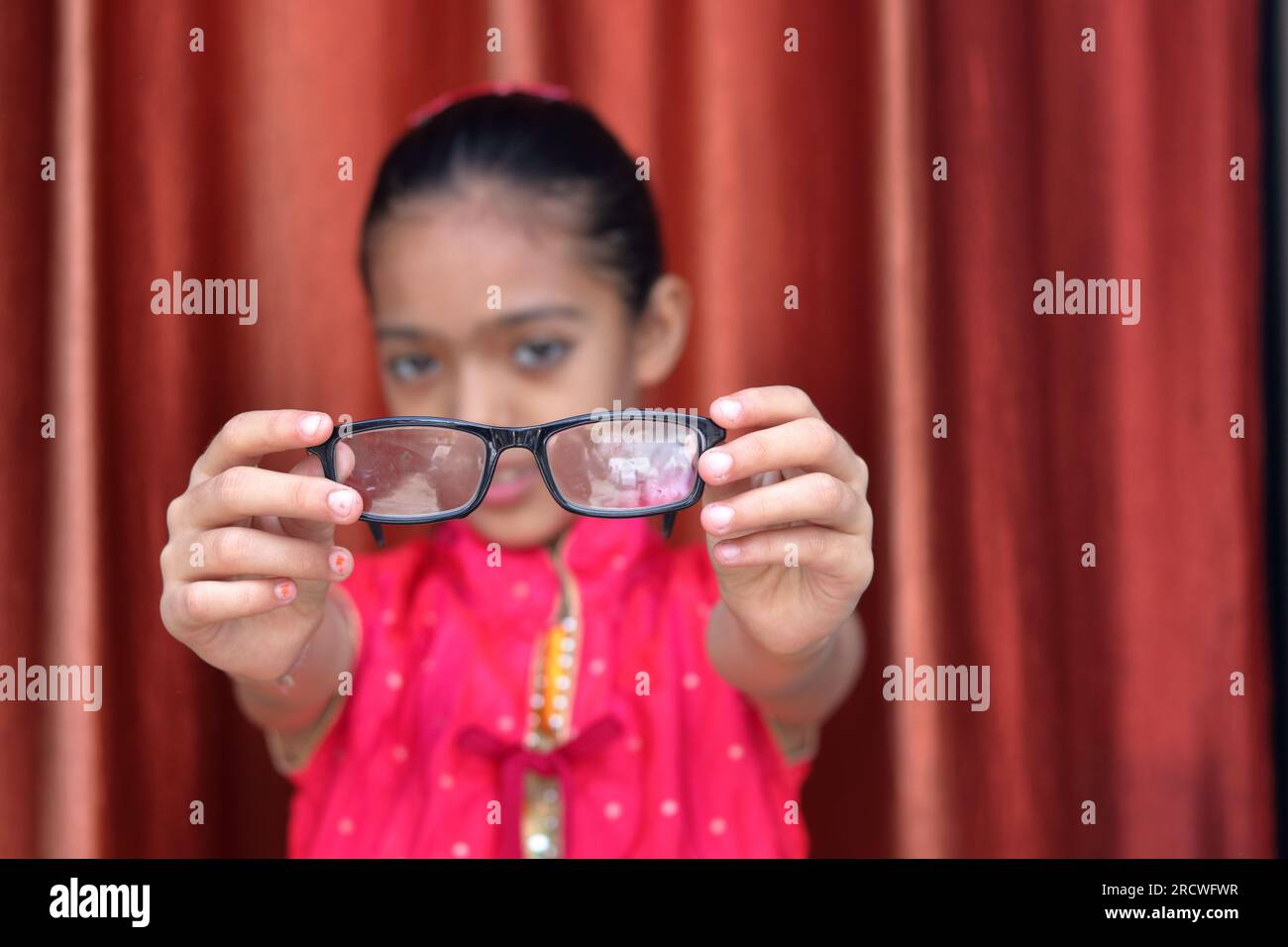 An Indian little pretty girl fiddling with her eye glasses in various poses in red dress. Stock Photo