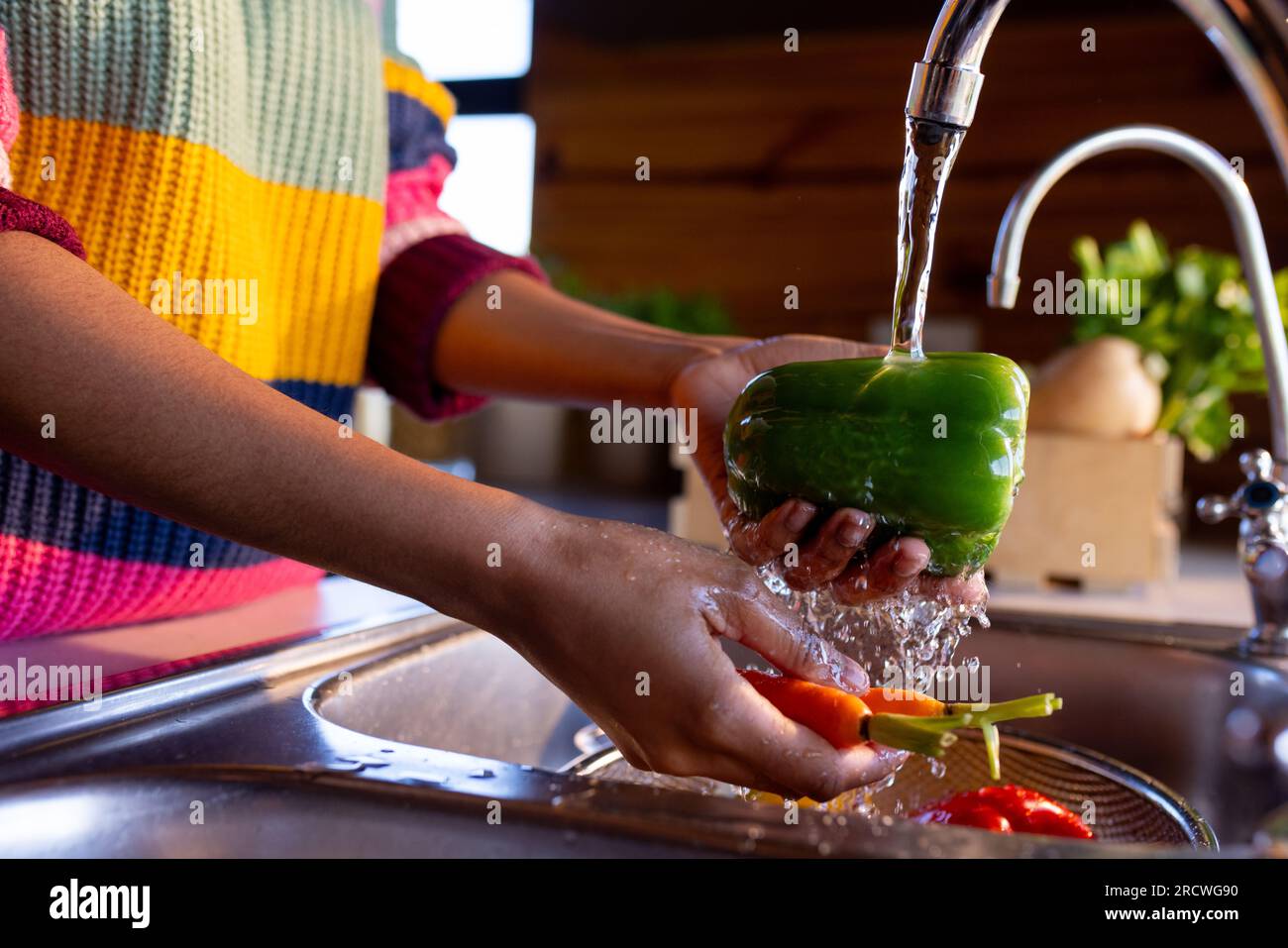 Midsection of african american woman preparing meal washing vegetables at sink in sunny kitchen Stock Photo
