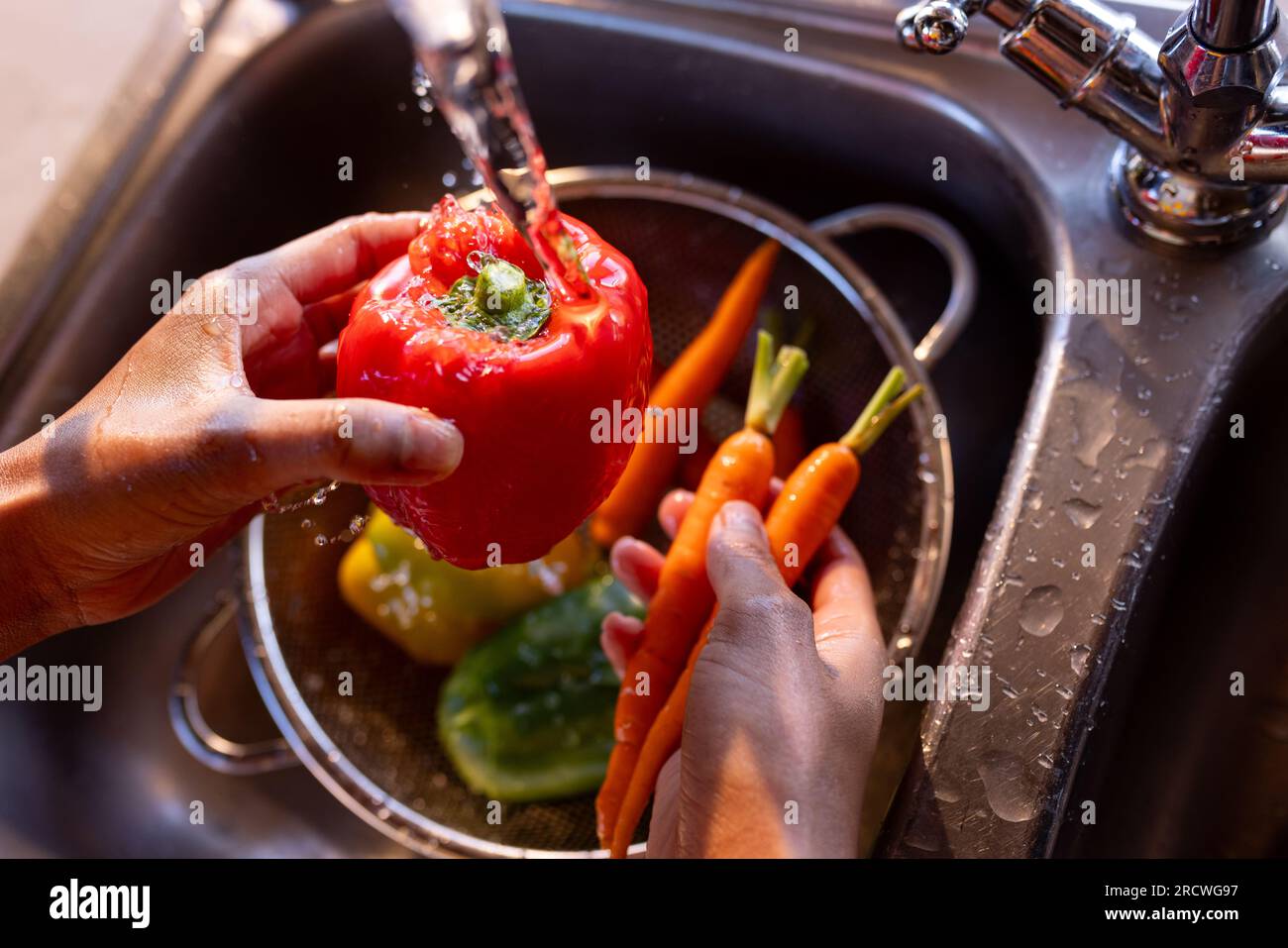 Hands of african american woman preparing meal washing vegetables at sink in sunny kitchen Stock Photo