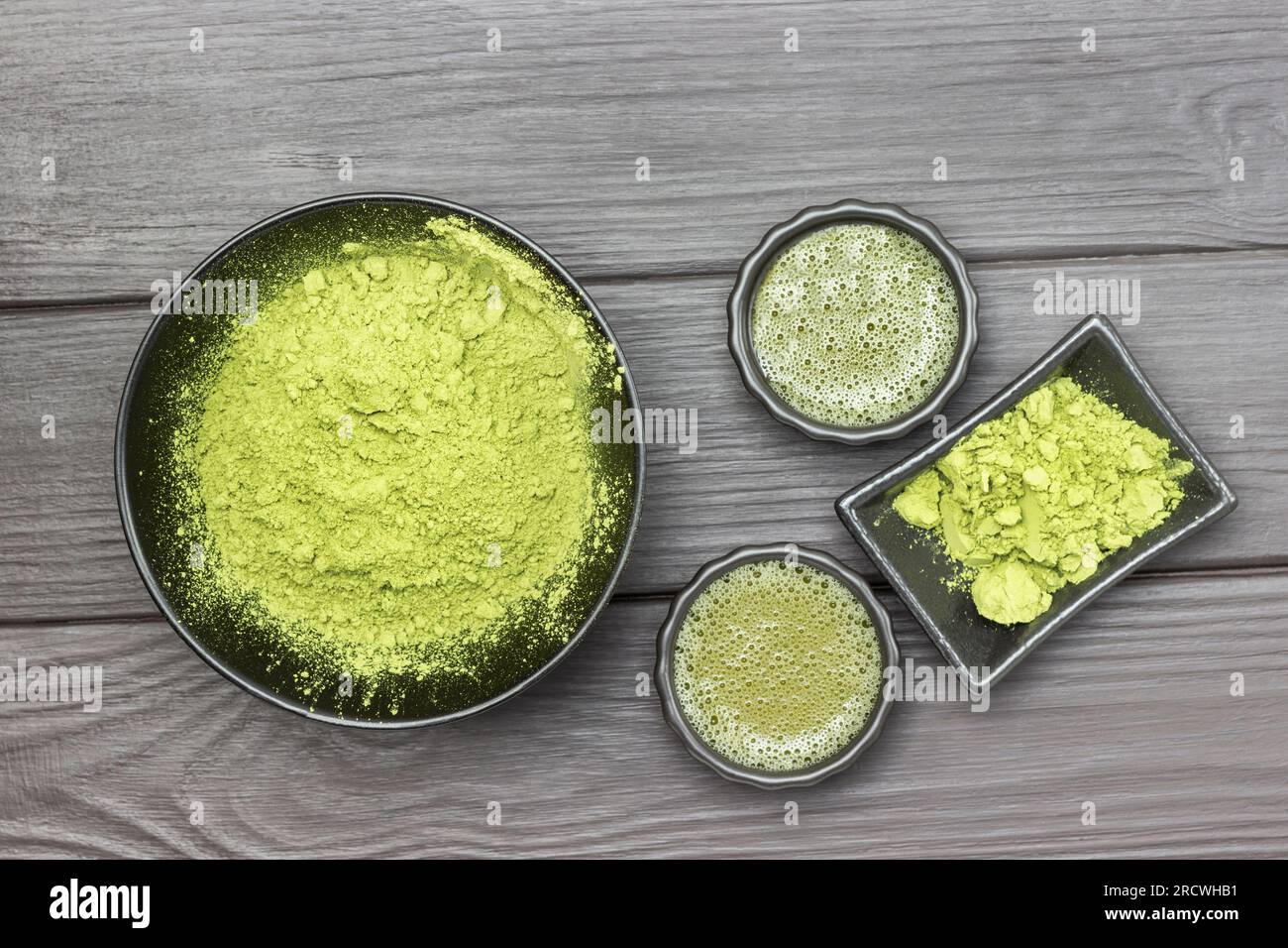 Matcha tea in two bowls. Green matcha tea powder in black bowl. Flat lay. Dark wooden background Stock Photo