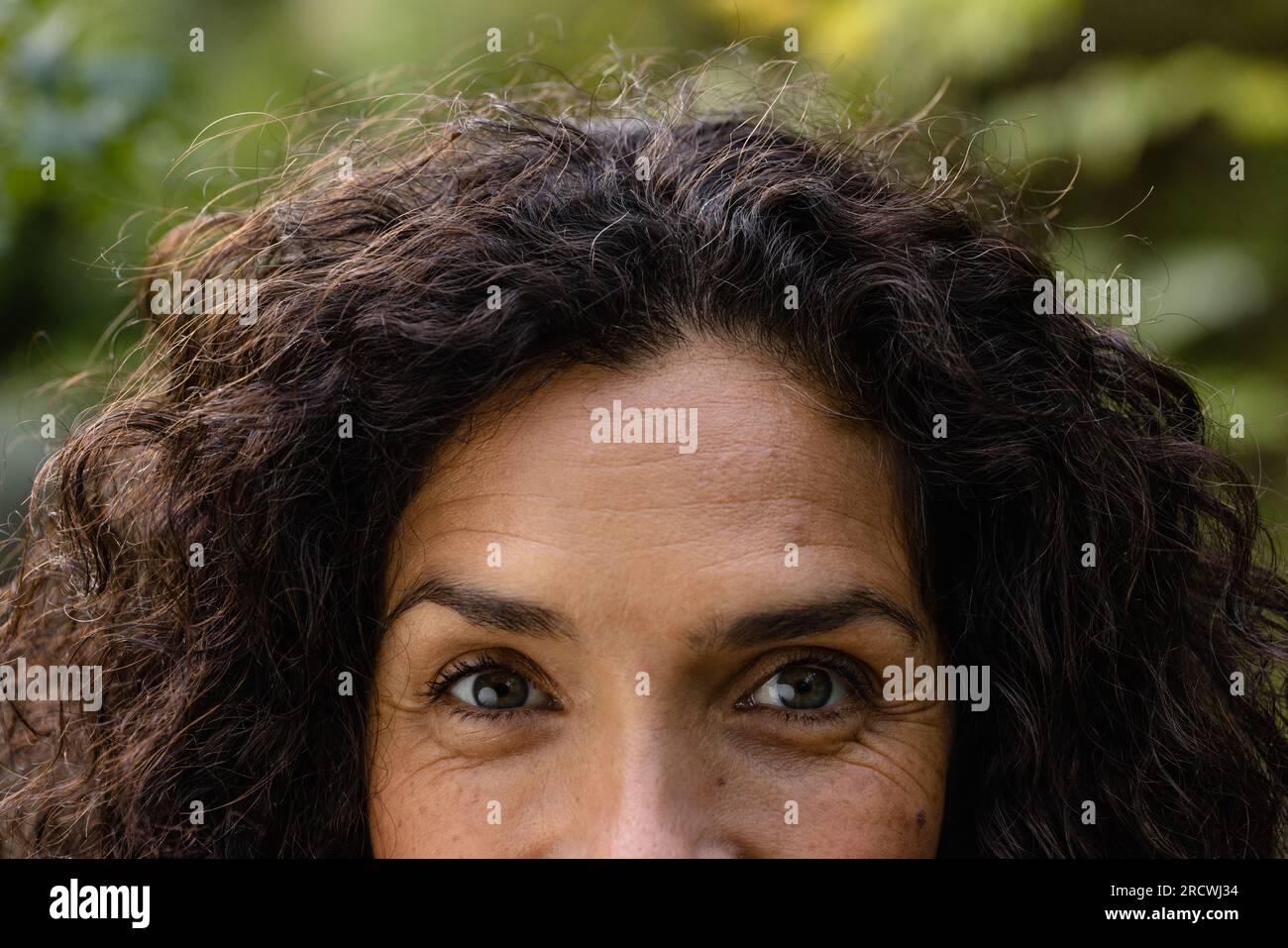 Portrait of happy biracial woman with dark curly hair smiling in garden Stock Photo