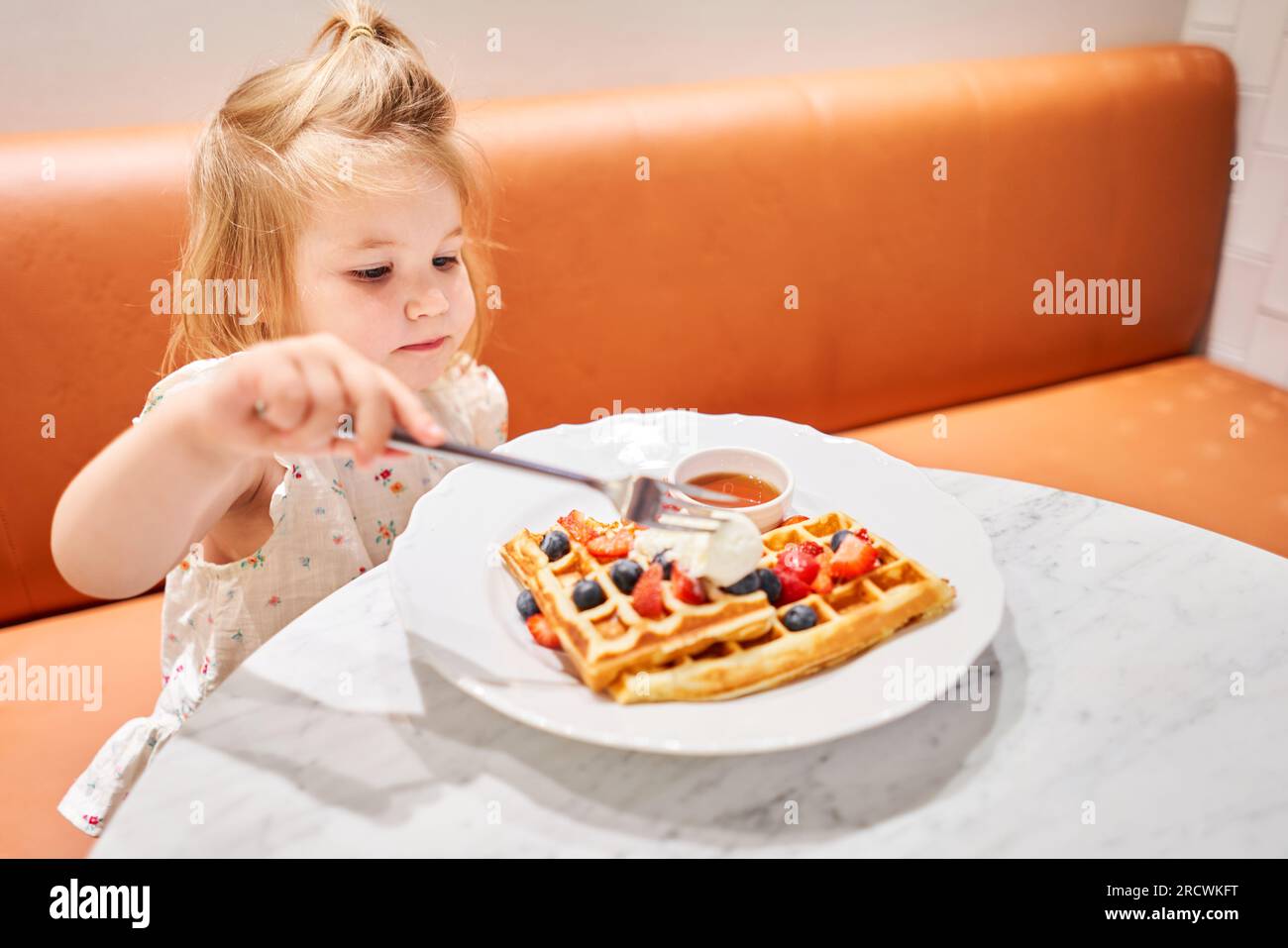 Happy 3 year old girl eat. Breakfast in cafe. Classic Viennese waffles