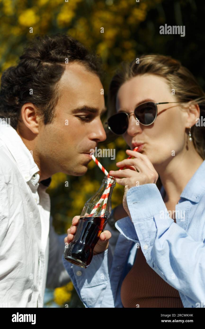 Young happy couple outdoors drinking cold drink from glass bottle with