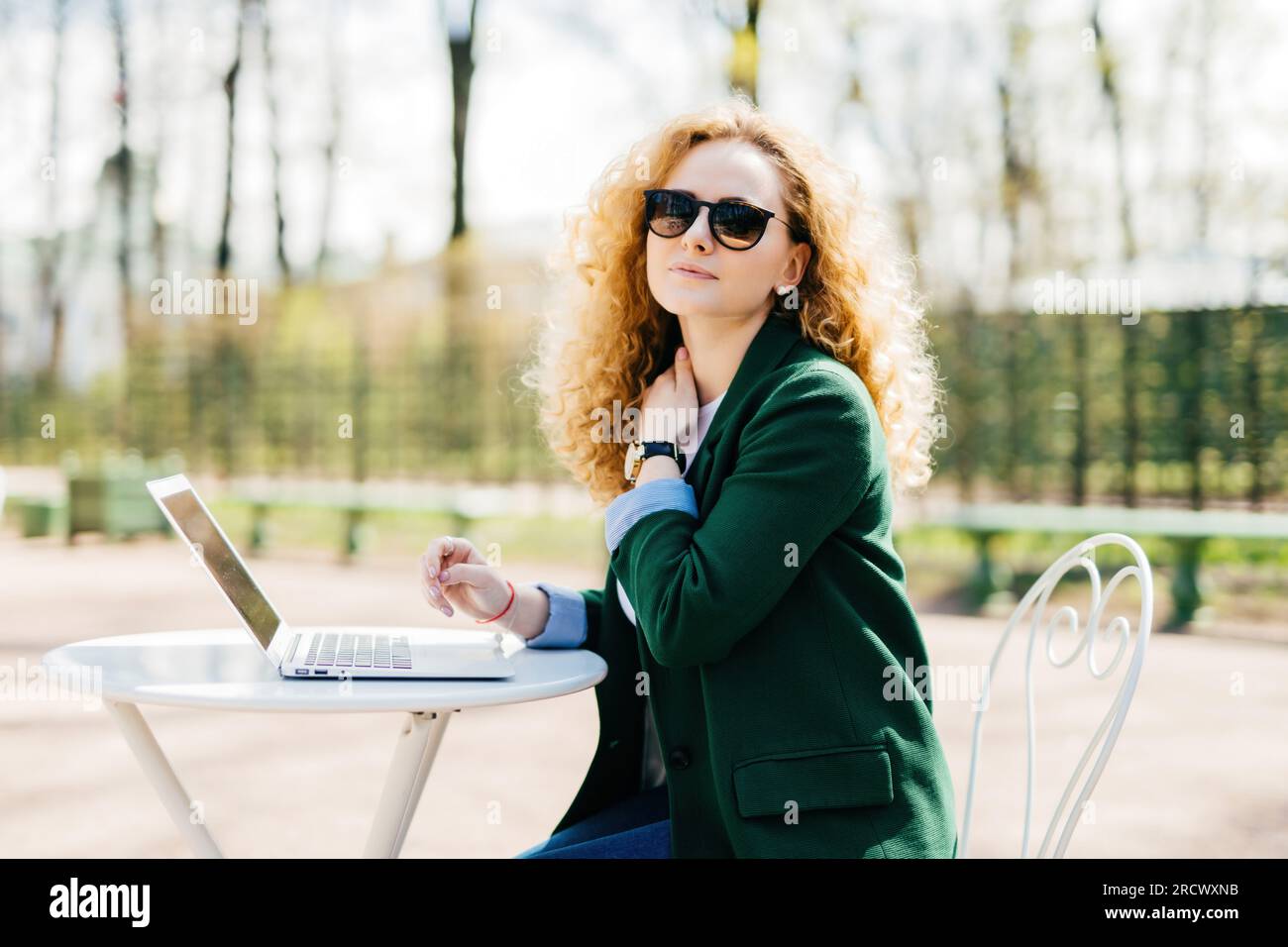 Exhausted freelancer, trendy clothes, fluffy blonde hair. Tired, isolated in nature, laptop, hand on neck. Stock Photo