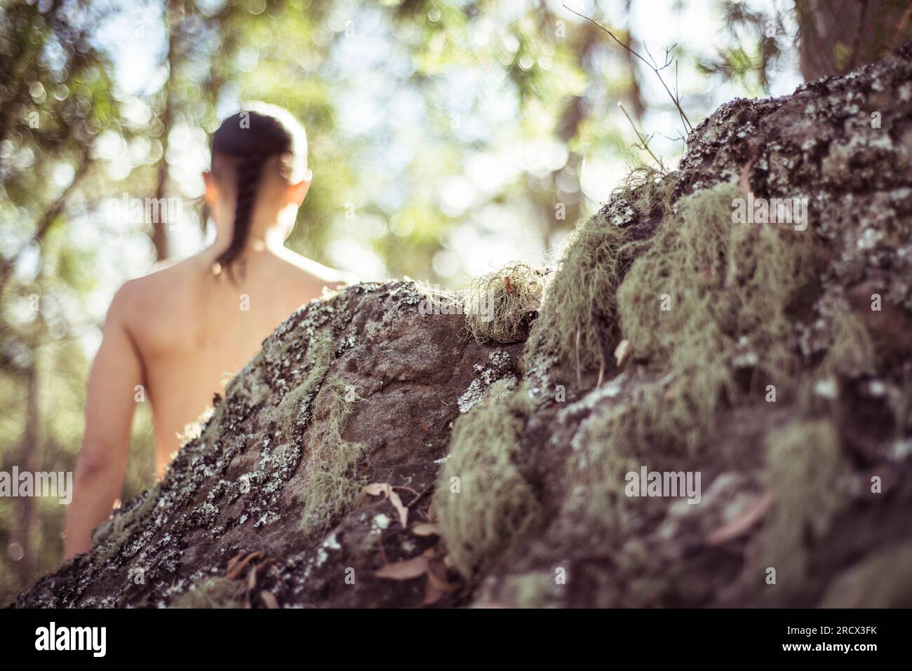 Ninja figure stands behind mossy rock in nature Stock Photo