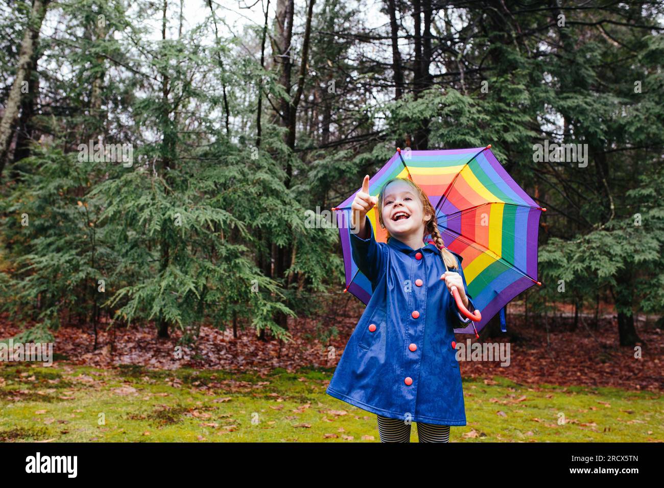 Young girl holding umbrella in a forest, pointing and smiling Stock Photo