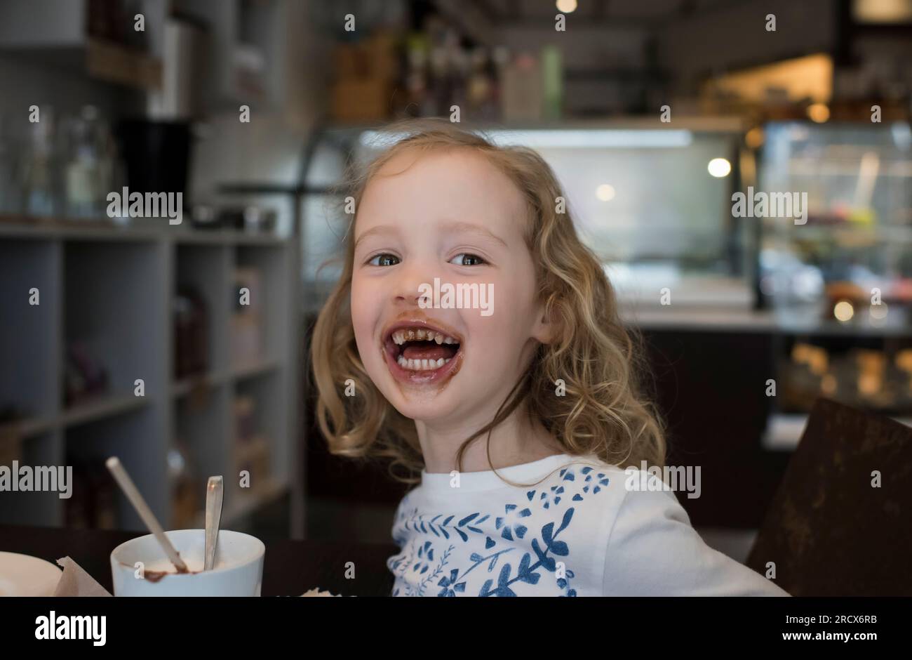 young girl sat in a cafe with chocolate around her mouth Stock Photo