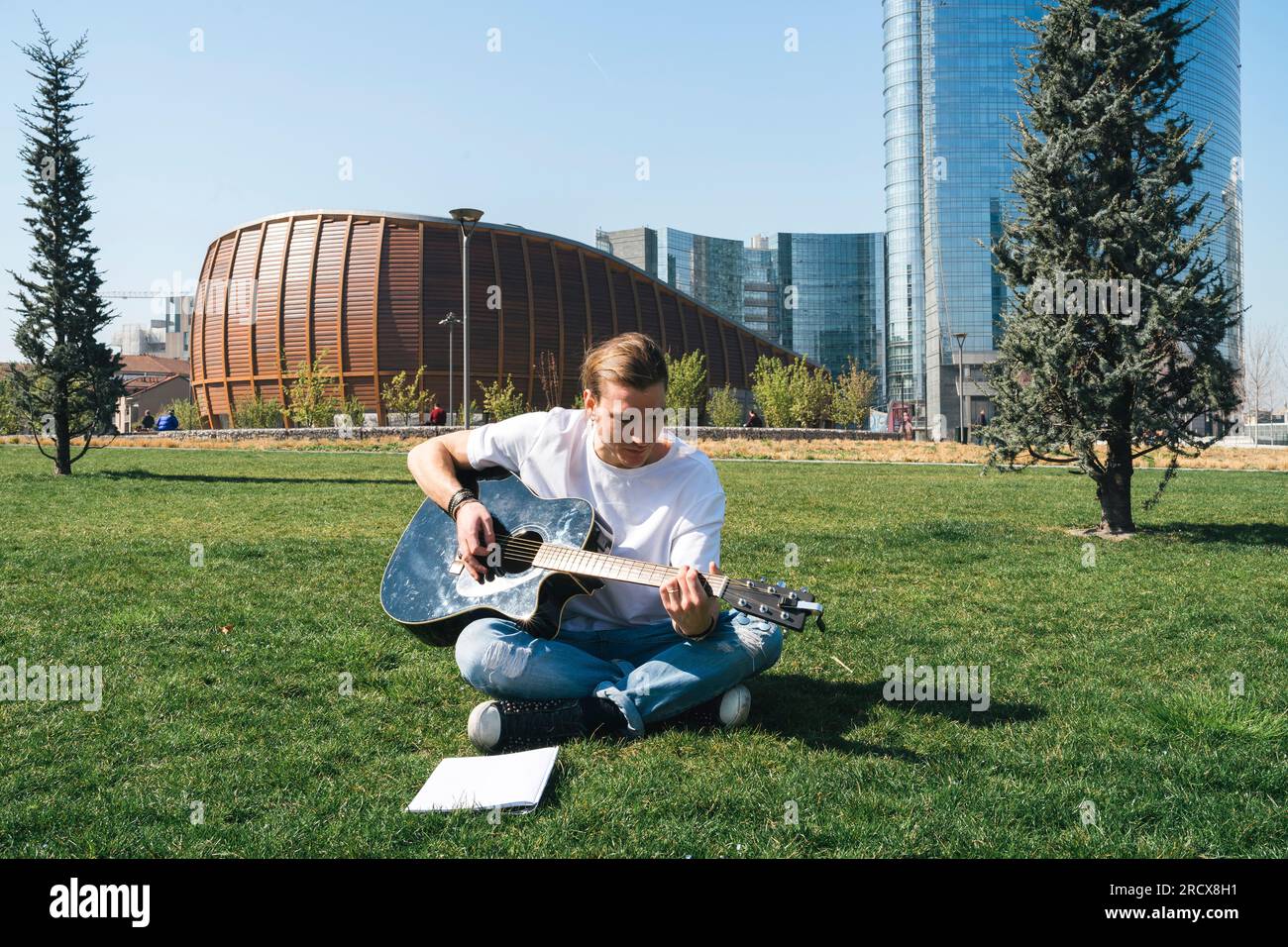 man studying music in urban garden playing guitar and reading script Stock Photo