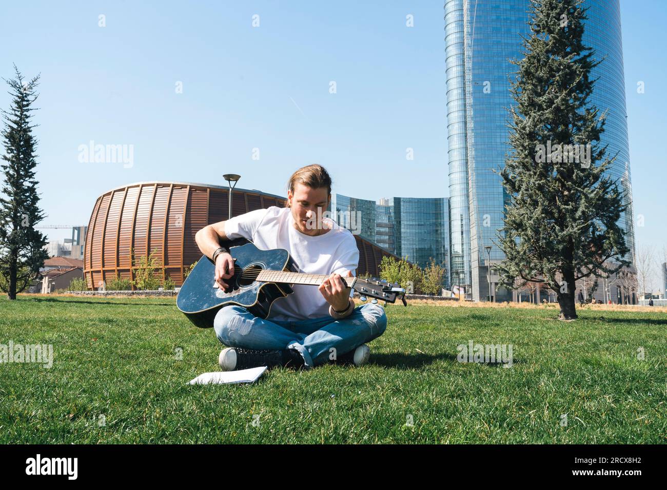 man composing music in urban garden playing guitar and reading script Stock Photo