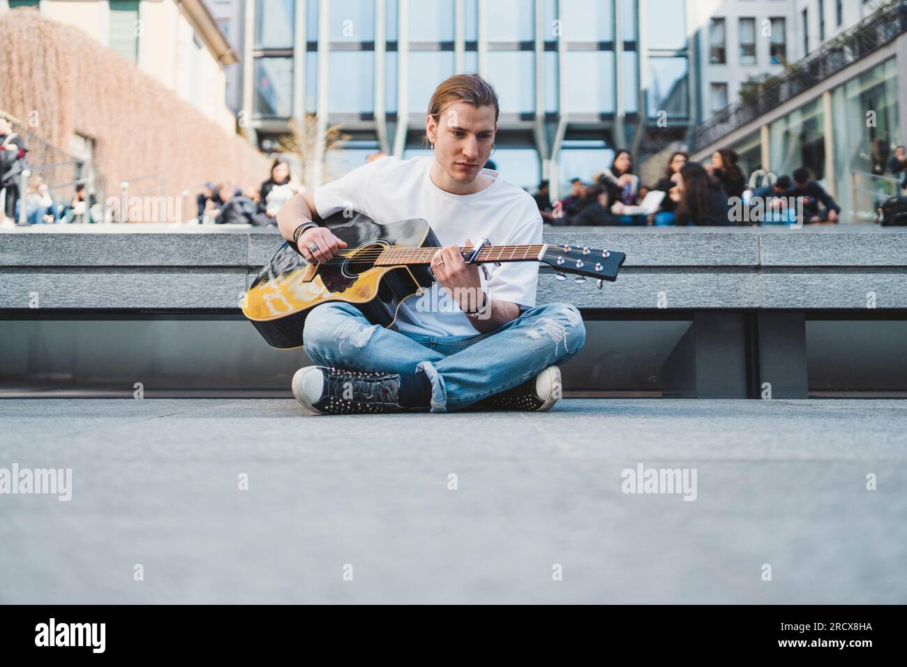 white musician sitting on the floor in a urban square with stone floor Stock Photo