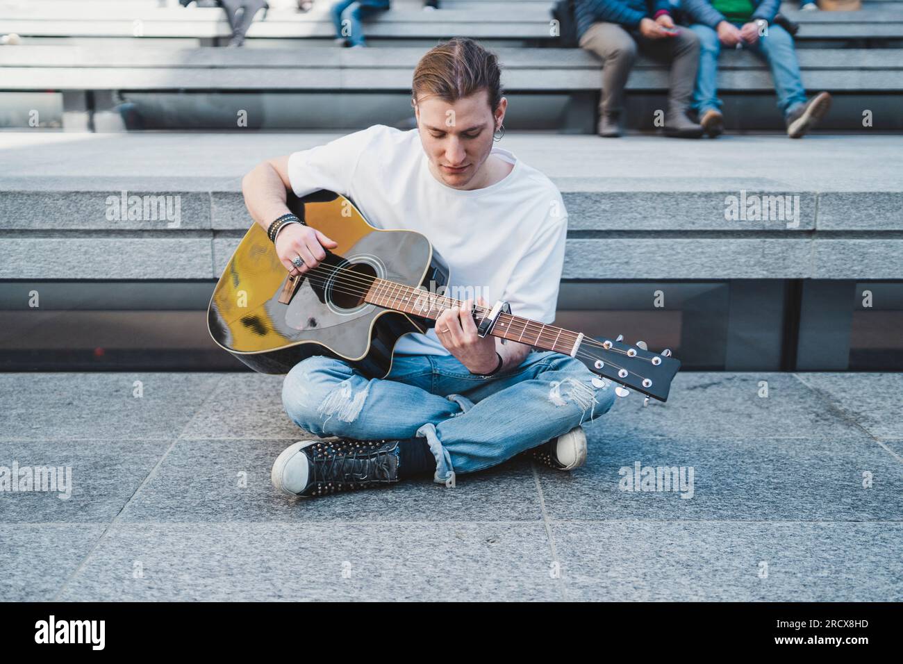 musician looking at the guitar sitting on the floor with people behind Stock Photo