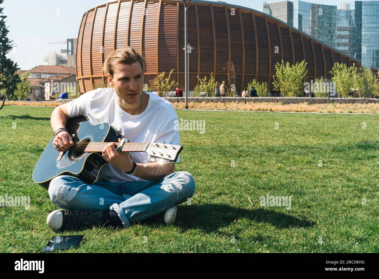 Young singer play the guitar in a urban garden during a sunny day Stock Photo