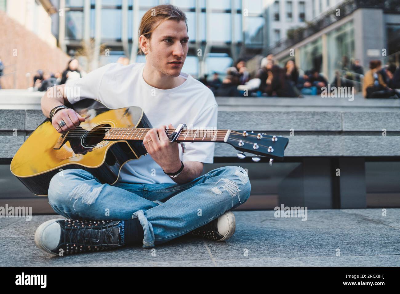 musician looking away is sitting on the floor with people behind Stock Photo