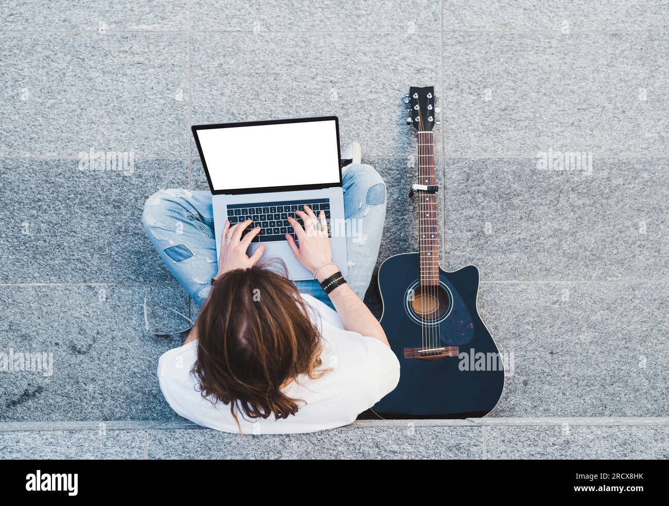 young man long hair writing on laptop sitting next acoustic guitar Stock Photo