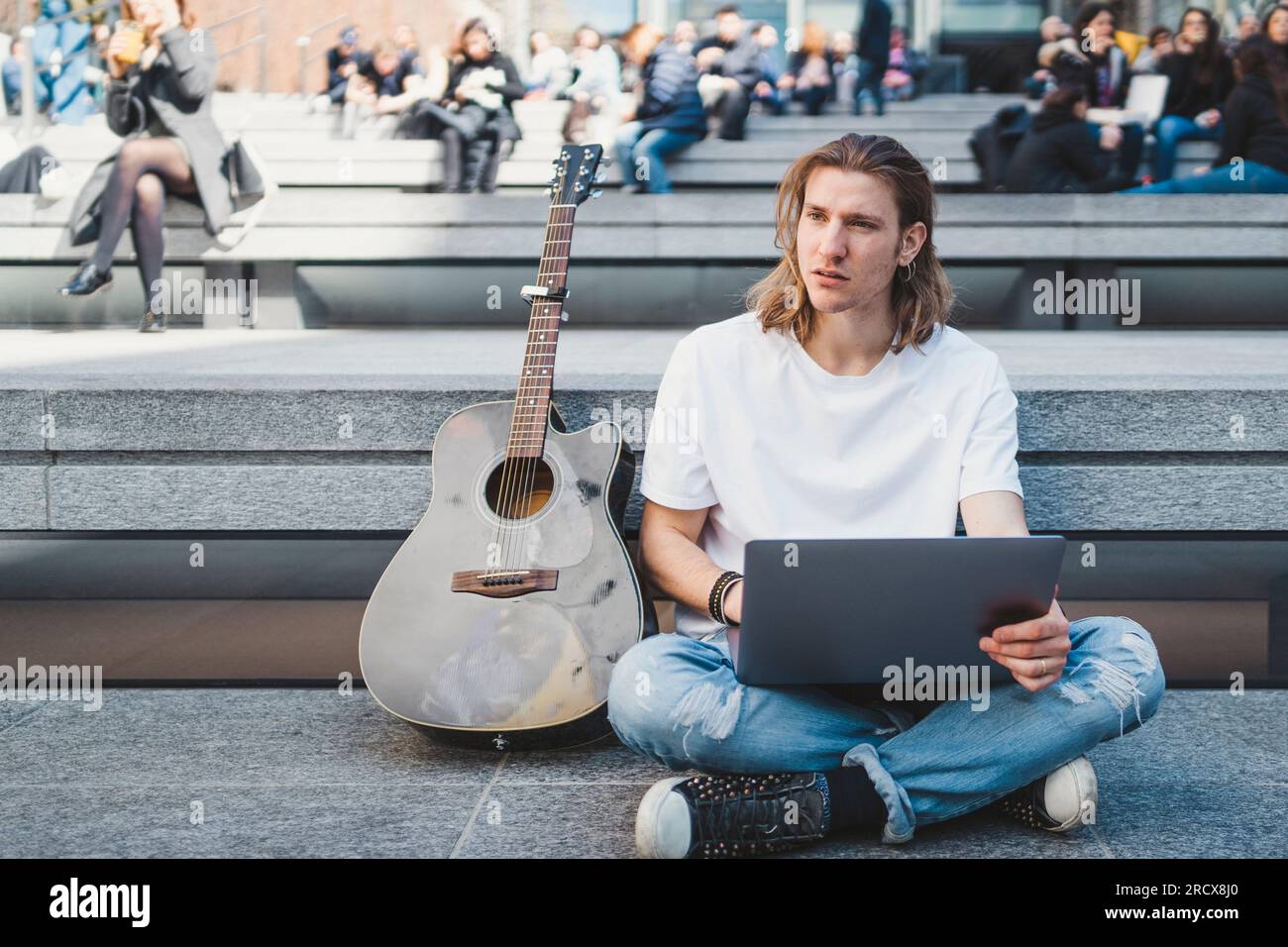 white man using laptop device outdoor next to his acoustic guitar Stock Photo