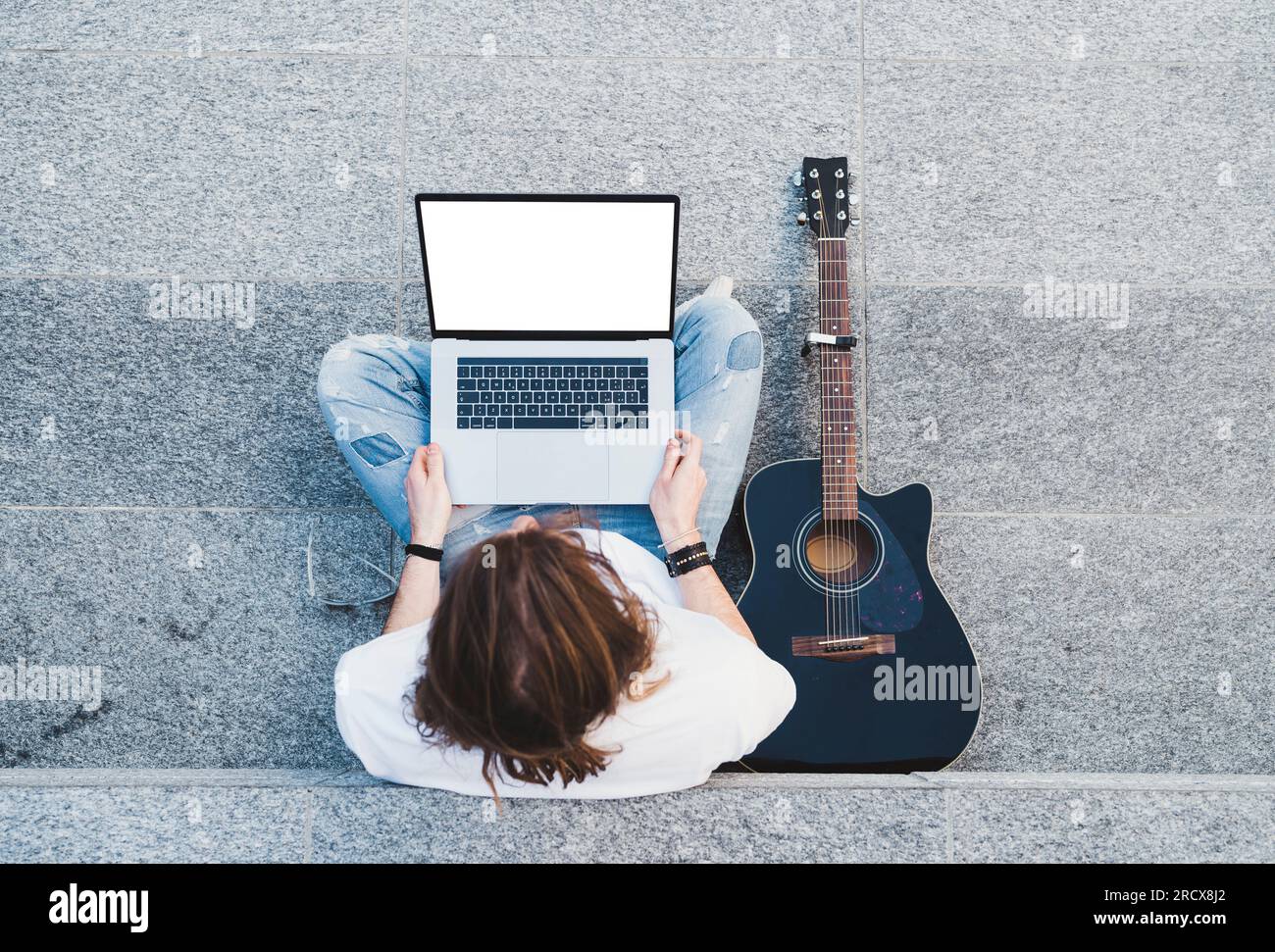 young man long hair holding laptop sitting next classical guitar Stock Photo