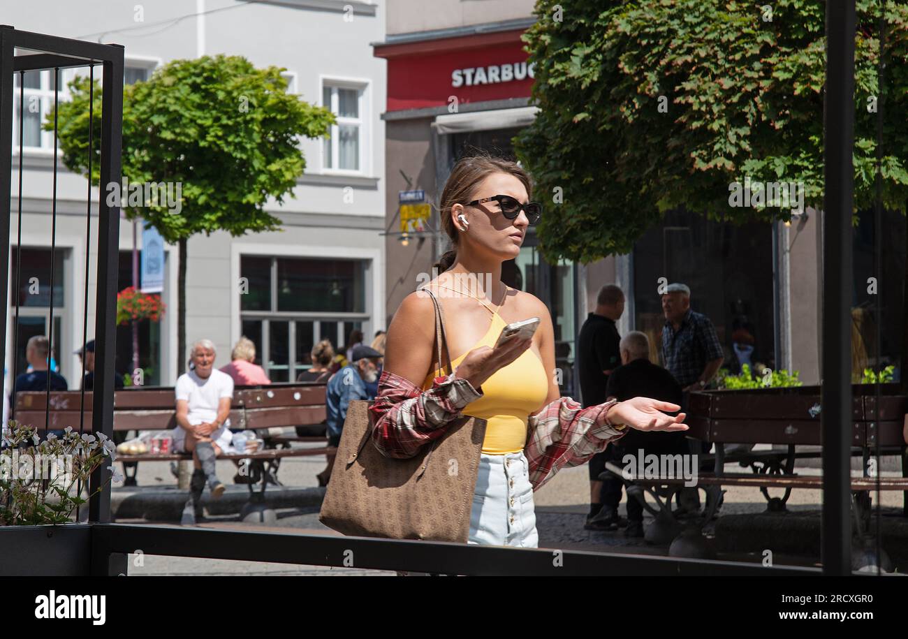 Attractive young woman, in yellow top, on mobile phone, in the street. Stock Photo