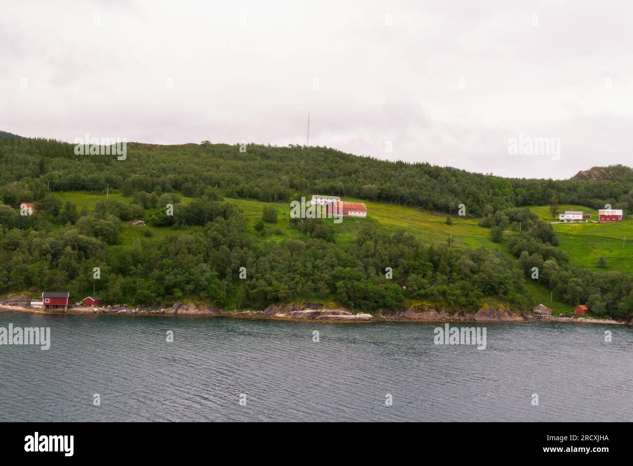 Small farms at the end of Holandsfjord with red fishing huts at edge of fjord close to Engen Brygge Svartigen Marina Norway Europe Stock Photo