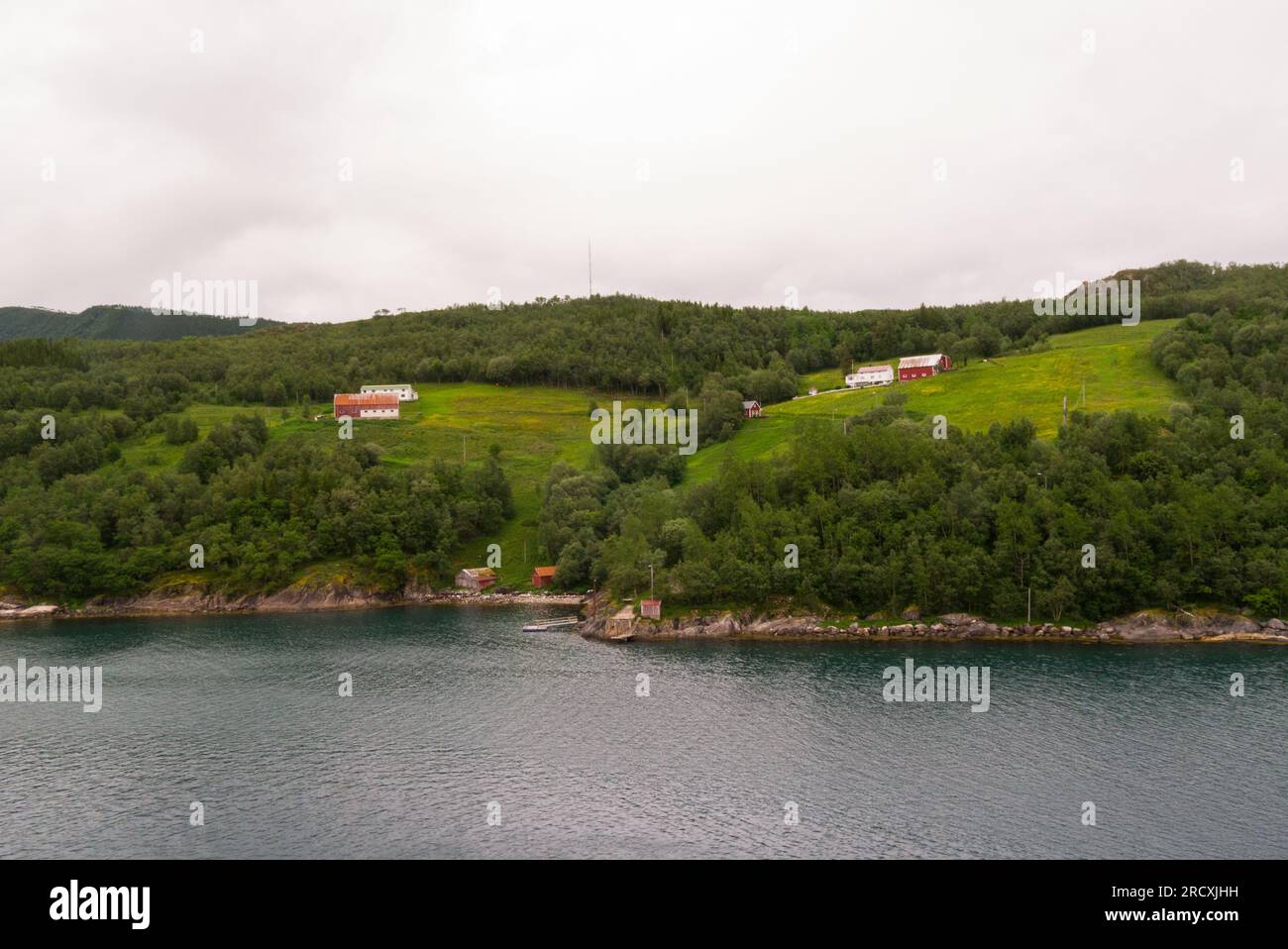 Small farms at the end of Holandsfjord with red fishing huts at edge of fjord close to Engen Brygge Svartigen Marina Norway Europe Stock Photo