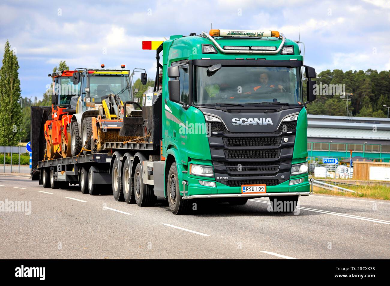Green Scania R650 truck transports roadworks asphalting machinery on flat trailer along highway 52. Salo, Finland. July 7, 2023. Stock Photo