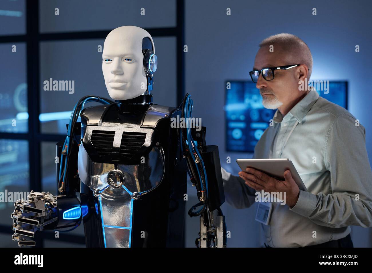 Mature engineer in eyeglasses using tablet pc to connect robot Stock Photo