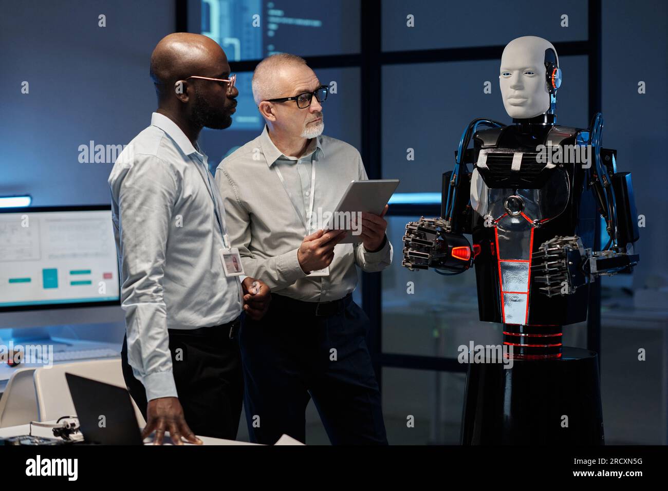 Two multiethnic engineers examining program of robot using digital tablet while standing in office Stock Photo