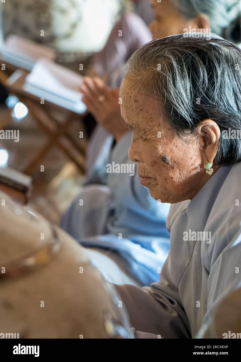 An elderly woman wearing jade earrings worships at Ling Ung Bai Buc Buddhist pagoda in Son Tra, Danang, Vietnam. Stock Photo