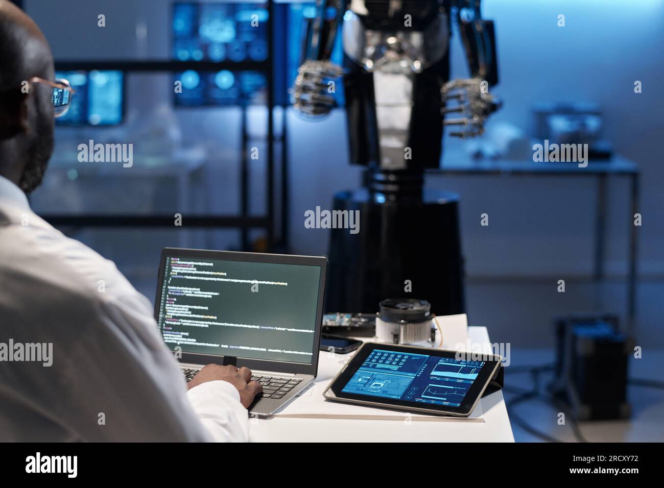 Rear view of engineer typing security codes on laptop to develop robotic industry Stock Photo