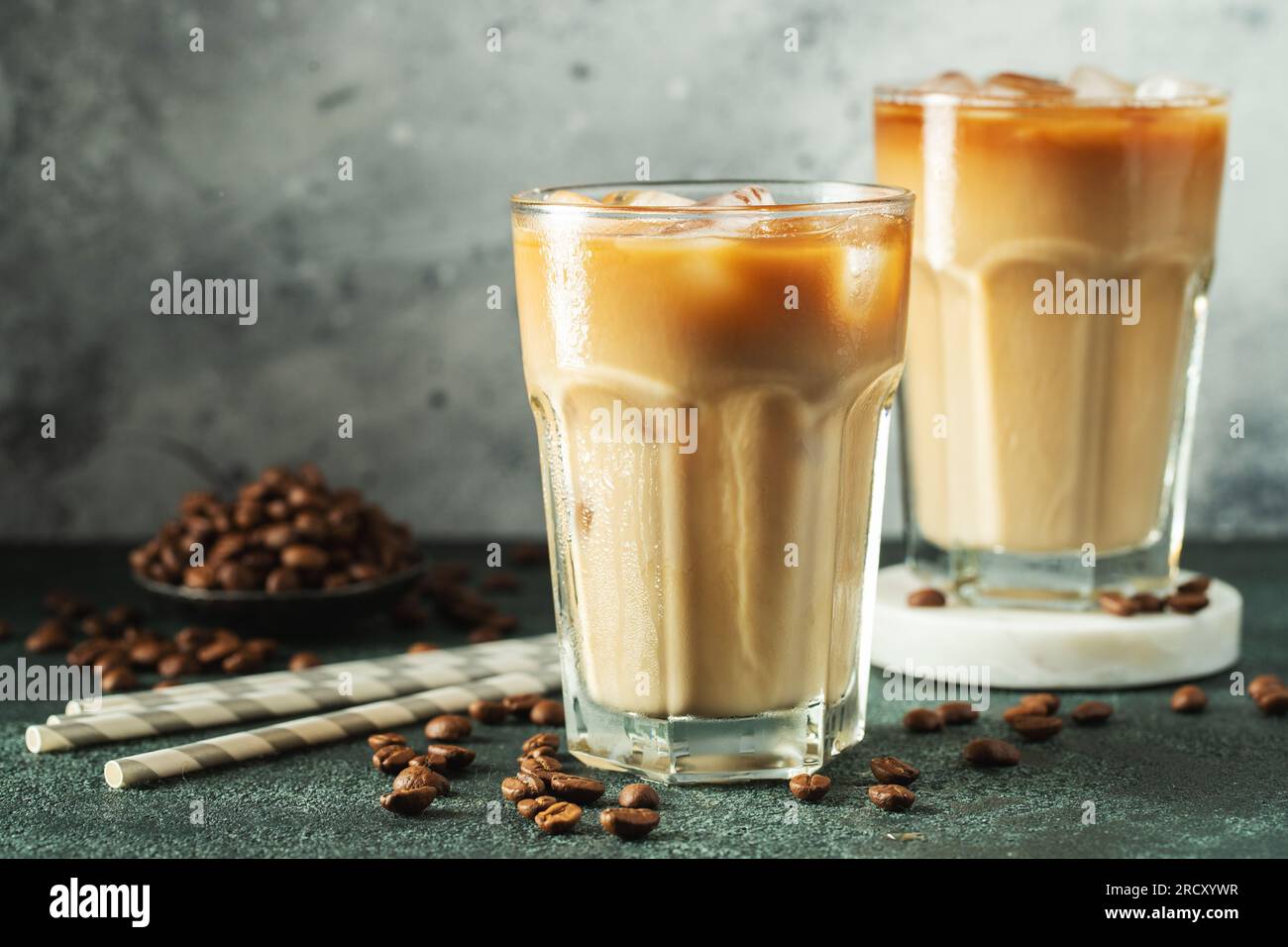 https://c8.alamy.com/comp/2RCXYWR/ice-coffee-in-a-tall-glass-with-cream-poured-over-ice-cubes-and-beans-on-a-dark-concrete-table-2RCXYWR.jpg