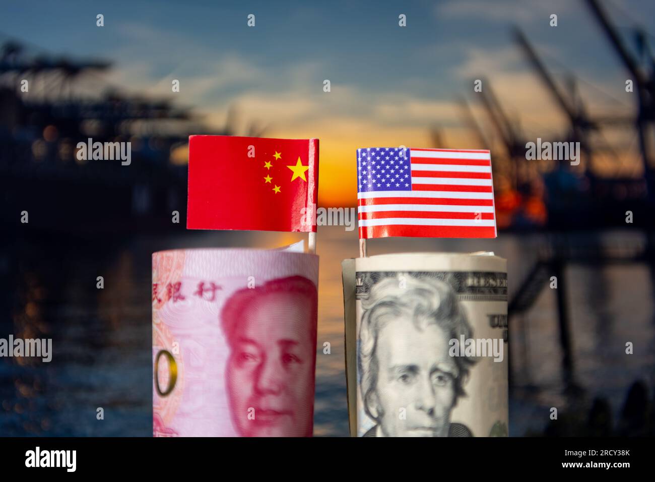 A roll of USD with the American flag and a bundle of Chinese Yuan and the Chinese national flag with a industrial background. A international trade de Stock Photo
