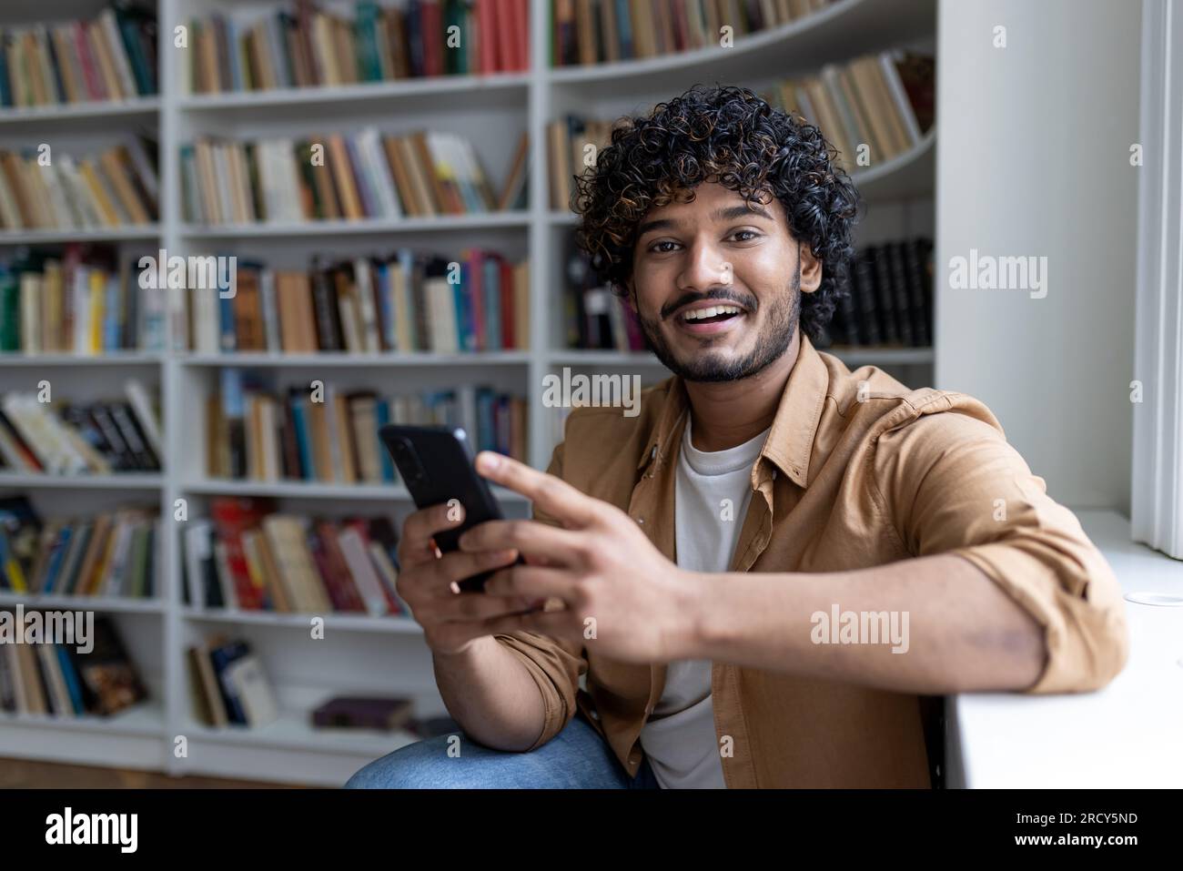 Portrait of young hispanic student, man holding phone smiling and ...