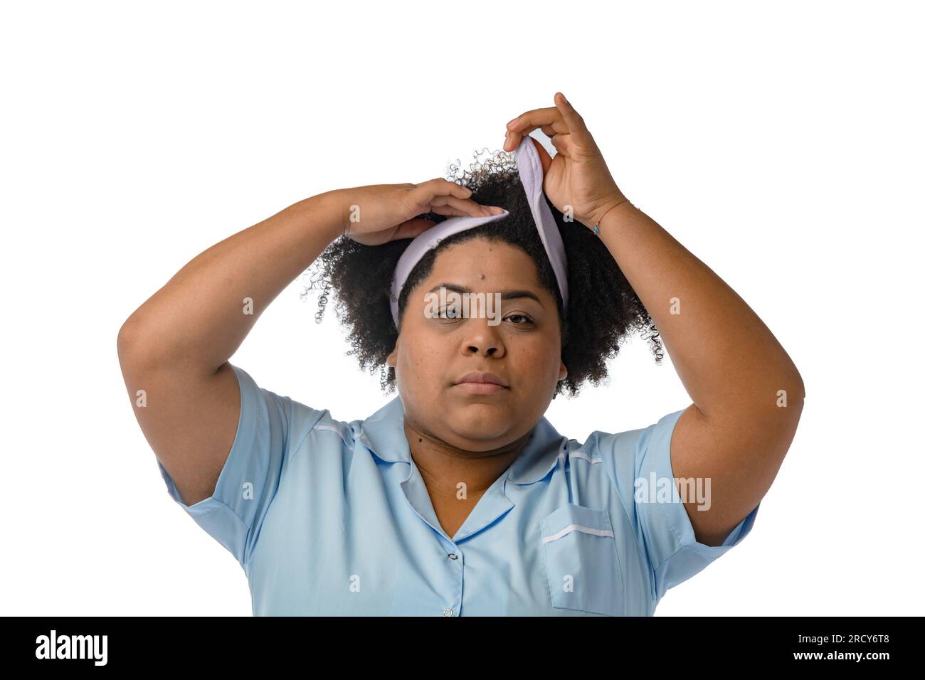 young afro latina brunette woman, putting on a head band for facial cleansing, looking at the camera, white background. Stock Photo