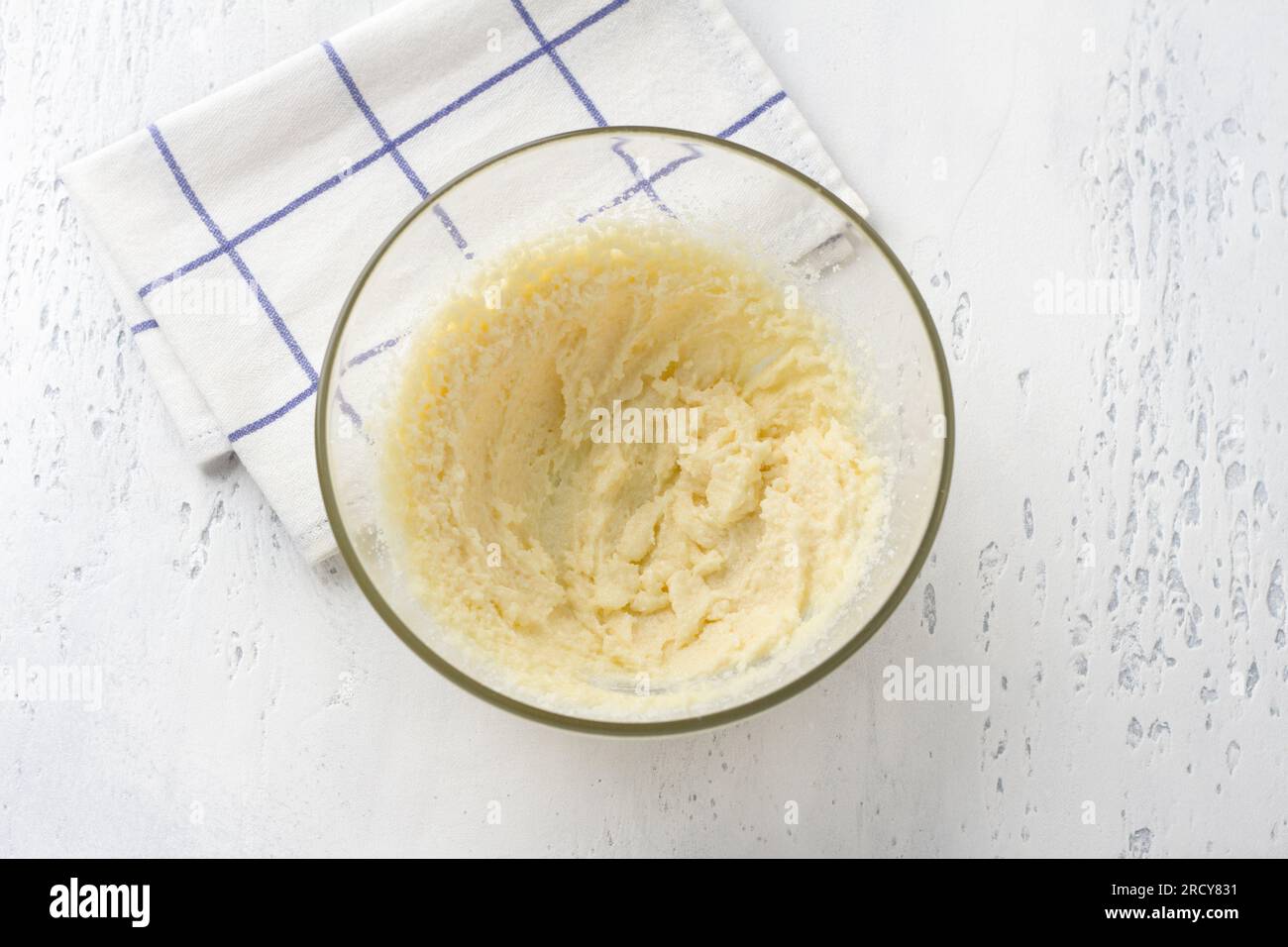 Glass bowl with whipped butter and sugar on a light blue background, top view. Cooking homemade milk cakes, do it yourself, step by step, step 2. Stock Photo