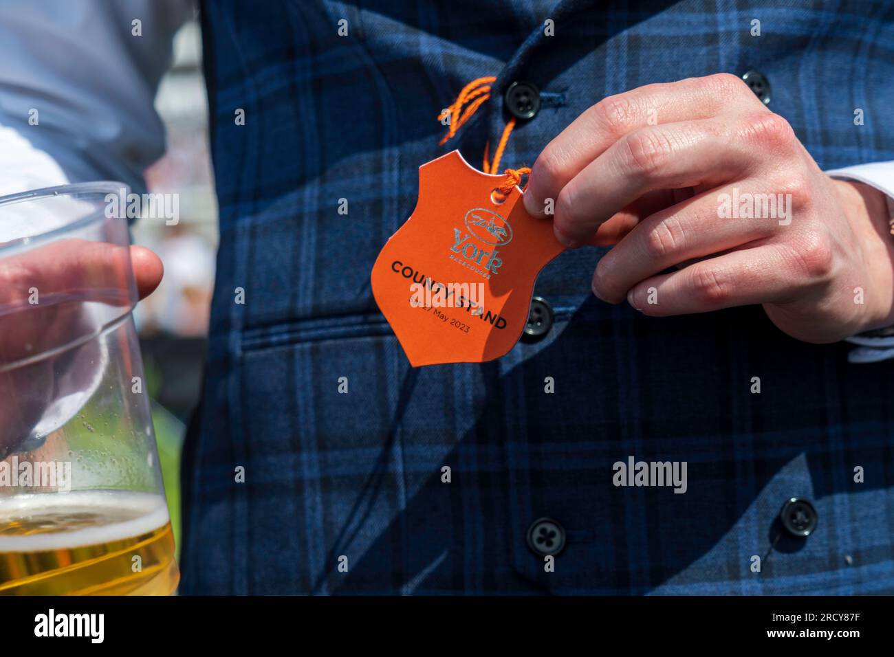 York horse race, a well-dressed man in an English style suit shows his pass for the York racecourse and his beer, during a popular horse racing event. Stock Photo