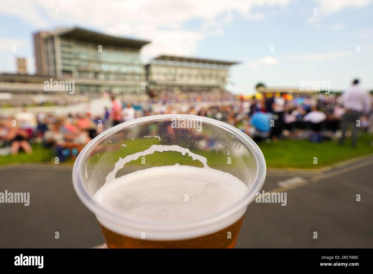 York Races, a plastic cup with beer, alcoholic beverage, with blurred unrecognizable crowds picnicking and racecourse grandstands in the background. Stock Photo