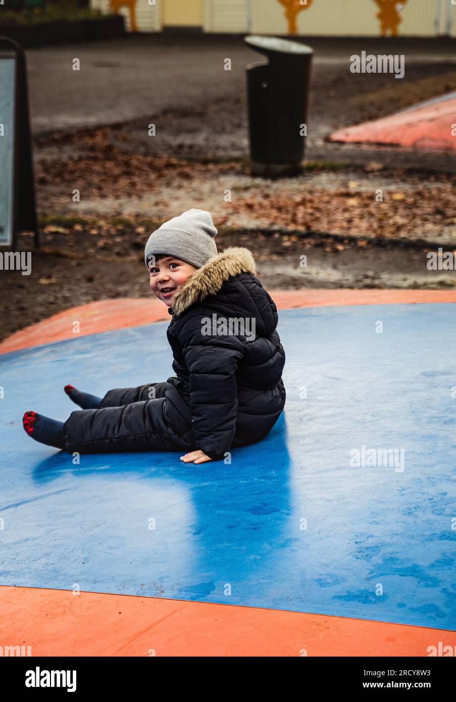 Mischievous smile of a boy sitting on a trampoline. Kid with cunning look laughing on a bouncer in a playground. Kid with cheerful smile or expression Stock Photo