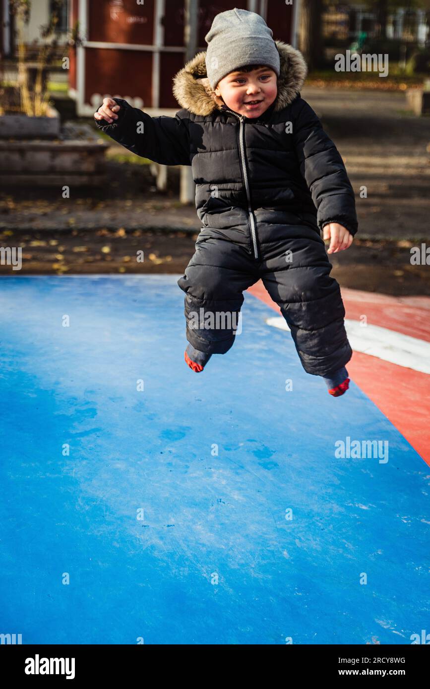 Happy child flying on a trampoline. Smiling kid jumping over an air bouncer. Boy has a cheerful or jovial expression playing. Healthy growth concept Stock Photo