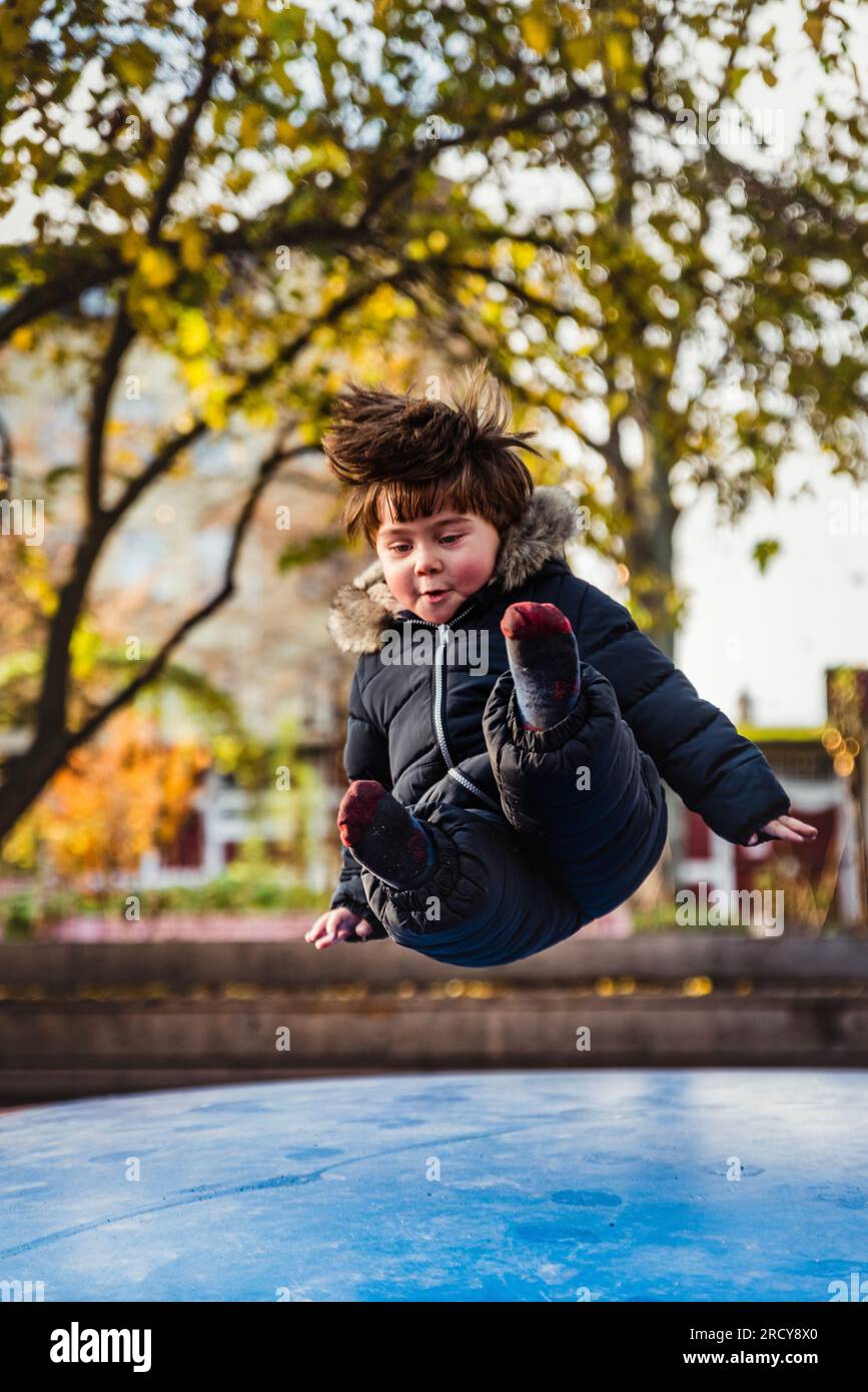 Child flying with joy on a soft trampoline. Boy jumping on a bouncer sitting in the air, landing on a morbid surface. Trust and security concept Stock Photo