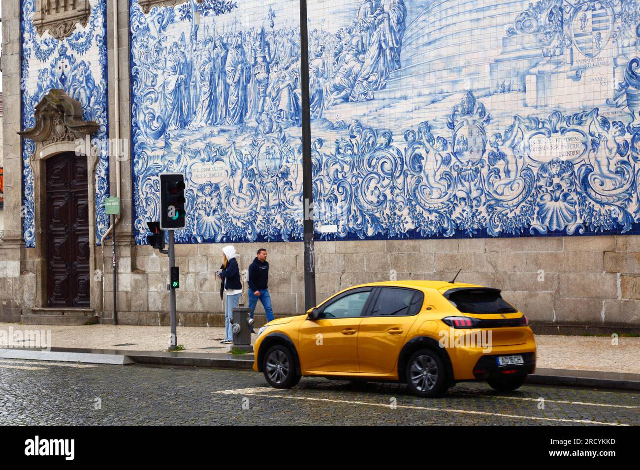 Yellow car driving past the azulejos / ceramic tiles on the side wall of Igreja do Carmo church, Porto / Oporto, Portugal Stock Photo