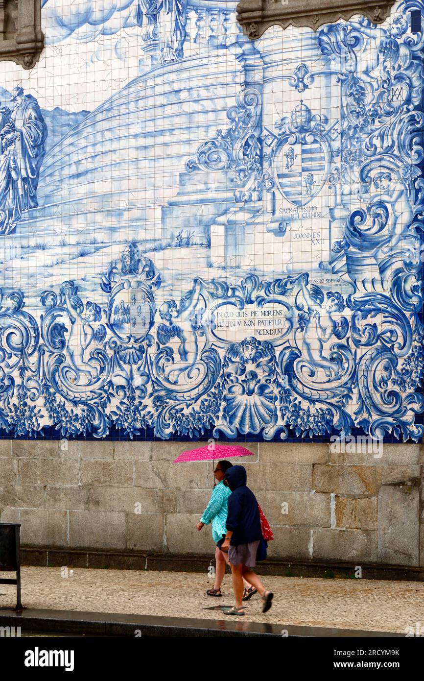 Female tourist carrying a pink umbrella walking past the azulejos / ceramic tiles on the side wall of Igreja do Carmo church, Porto / Oporto, Portugal Stock Photo