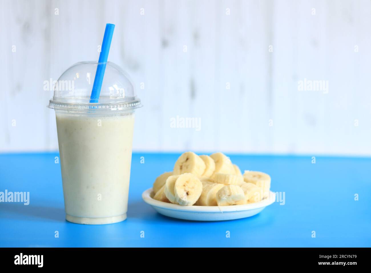 https://c8.alamy.com/comp/2RCYN79/banana-smoothie-with-a-plastic-disposable-cup-a-plate-with-a-sliced-banana-next-to-it-banana-milkshake-2RCYN79.jpg