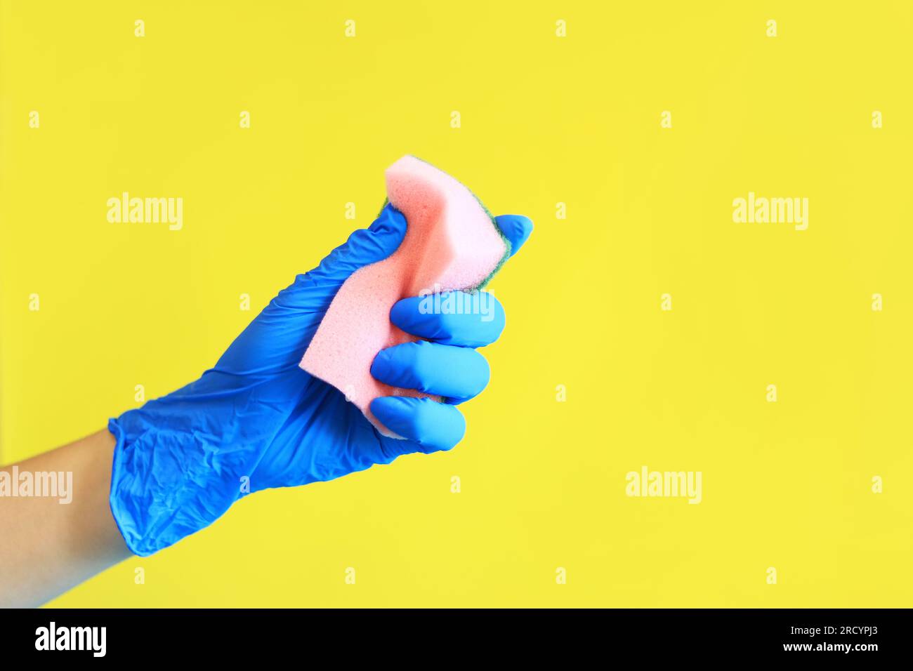 A woman's hand in a blue glove squeezes a sponge for washing dishes