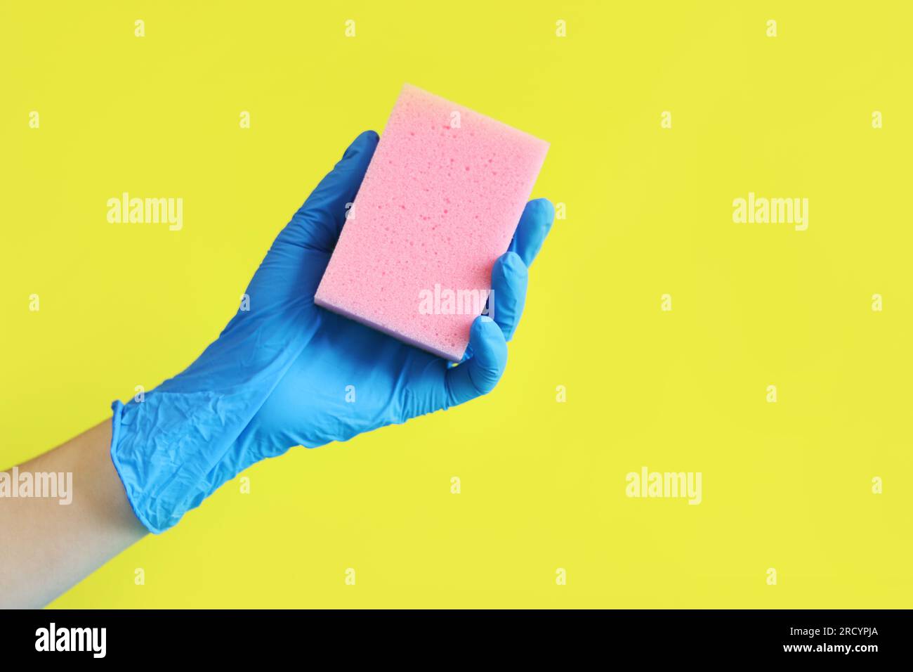 A woman's hand in a blue glove holds a sponge for washing dishes. House
