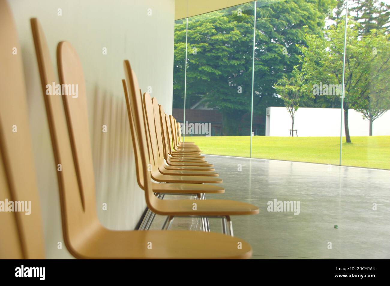 Wooden chairs in a row looking out of a window. Contemplation space, empty chairs waiting to be occupied, ideal to represent the idea of meeting peopl Stock Photo