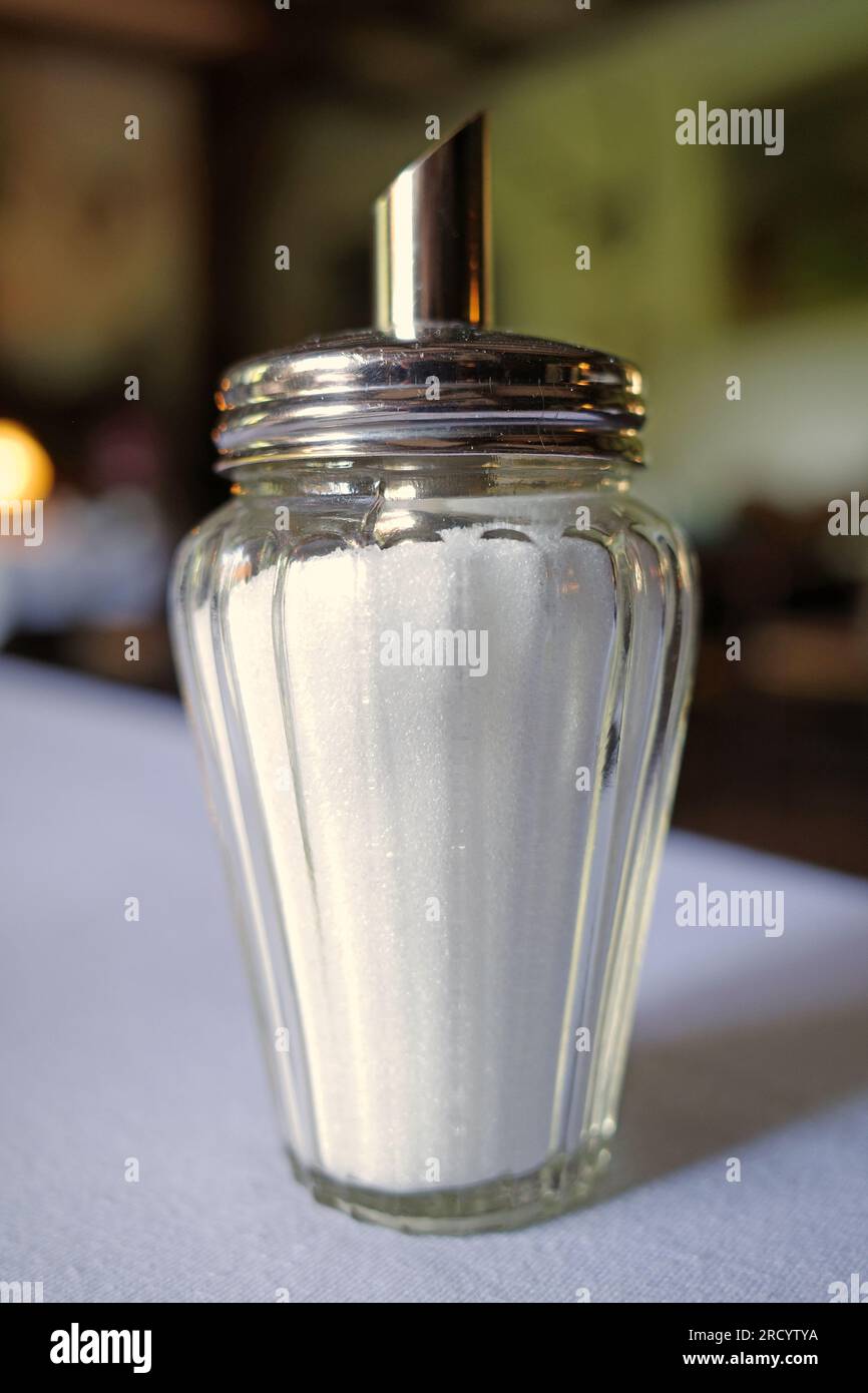 A traditional glass sugar dispenser with a steel lid filled with white