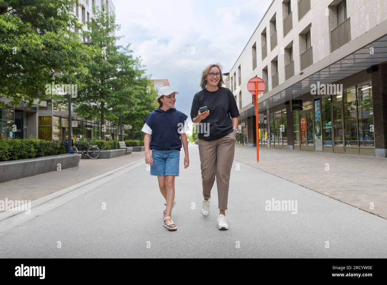 Happy mom and daughter walking on the street with shops Stock Photo