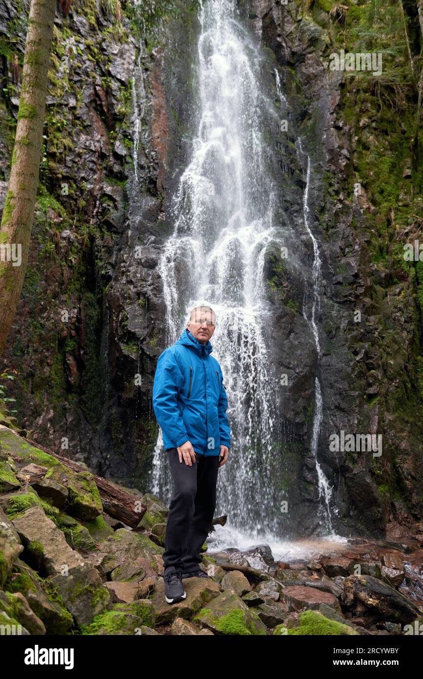 Tourist attraction of Germany - falls of Burgbach Waterfall near Schapbach, Black Forest, Baden-Wurttemberg, Germany. Man hiker in blue jacket standin Stock Photo